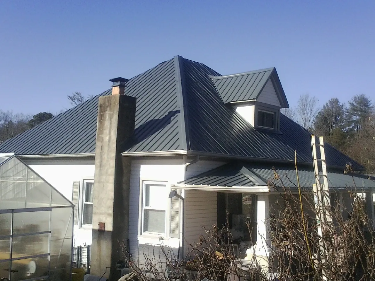 Dark blue standing seam metal roof on a white farmhouse with dormer — Slate & Tile Roof Repair by Roofing Brothers in Dola