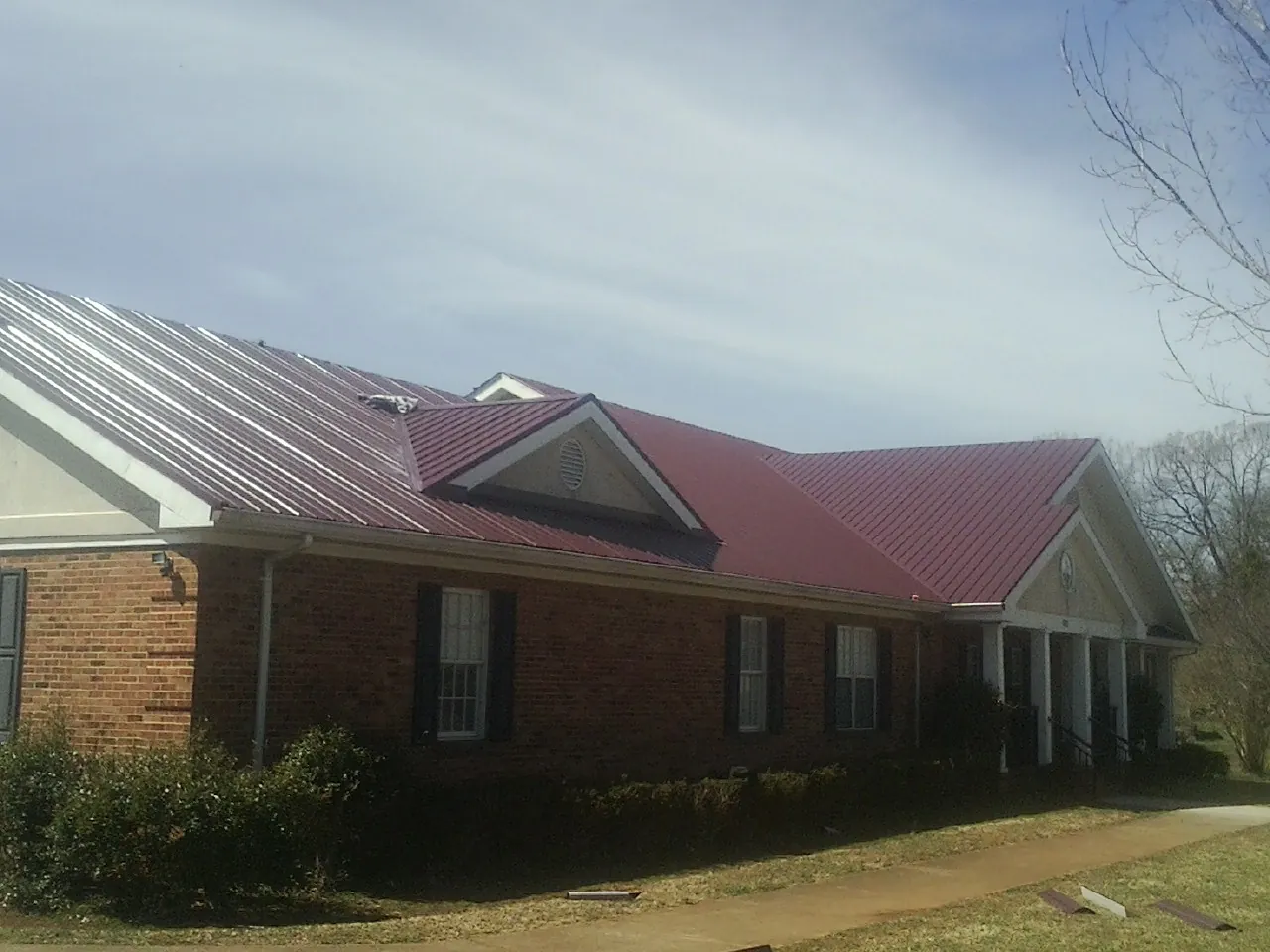 Red metal roof with gabled entries on a long brick building, from a Hail Damage Roof Repair job in Dola