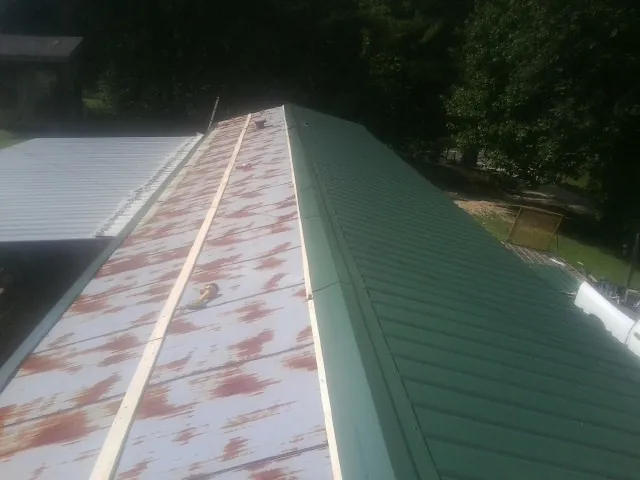 Old rusted panels beside newly installed green metal roofing — Wind Damage Roof Repair by Roofing Brothers in Dola