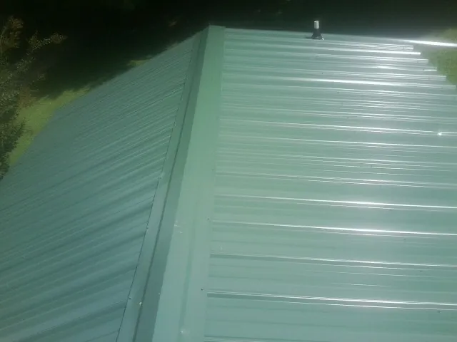 New green metal panels meeting at the ridge of a roof — Flat Roof Repair work by our crew in Dola