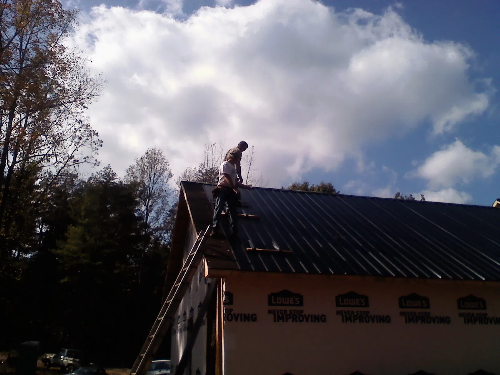 Roofer fastening dark metal panels high against a cloudy sky, from a Roof Inspection job in Dola