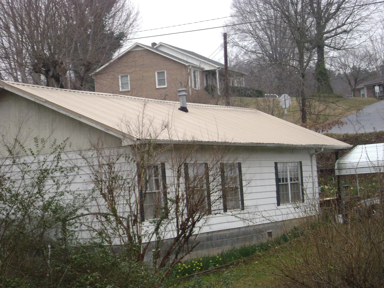 Tan metal roof on a white sided house set into a hillside — Commercial Roofing by Roofing Brothers in Dola